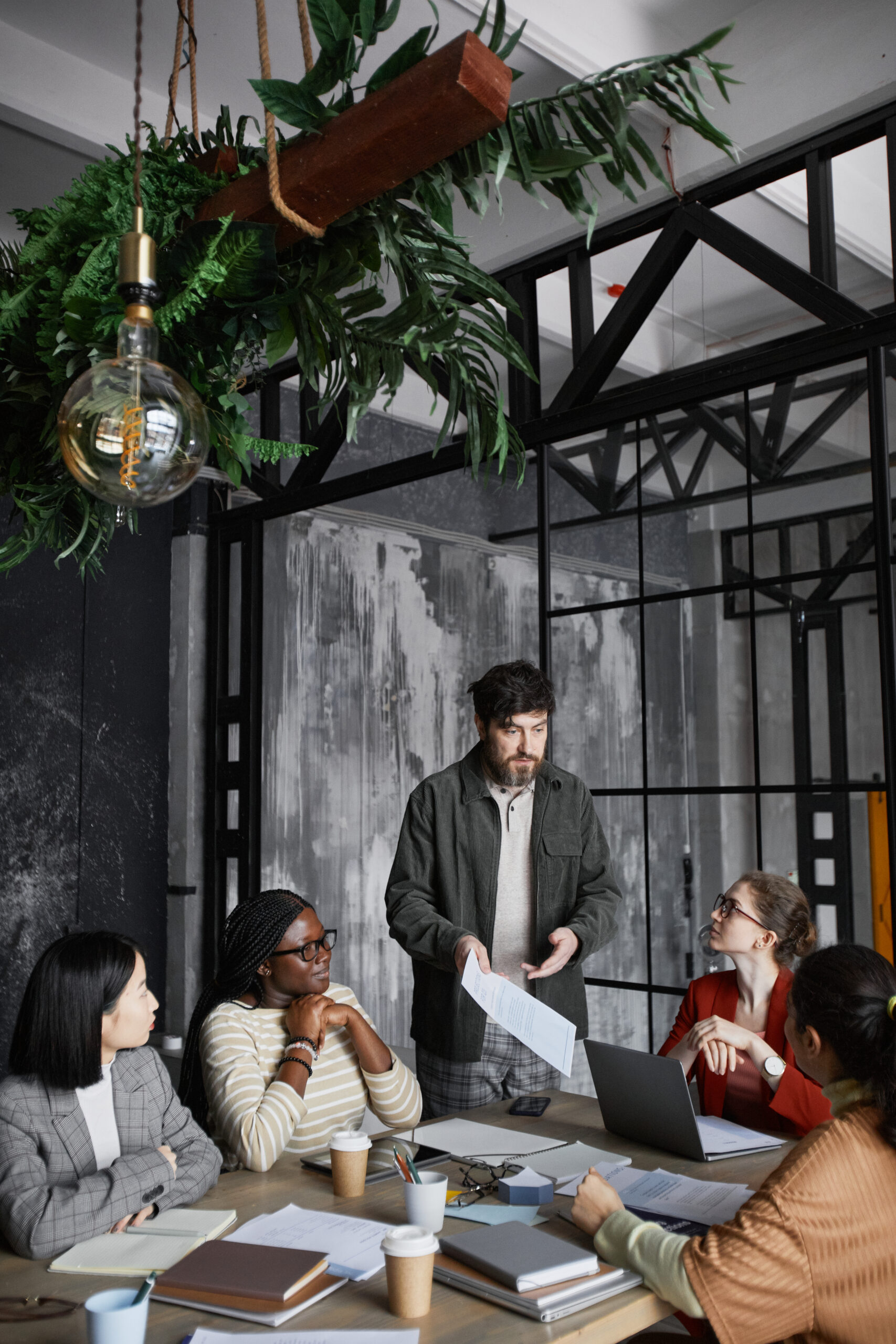 Vertical portrait of bearded businessman giving presentation to colleagues during meeting in office, copy space